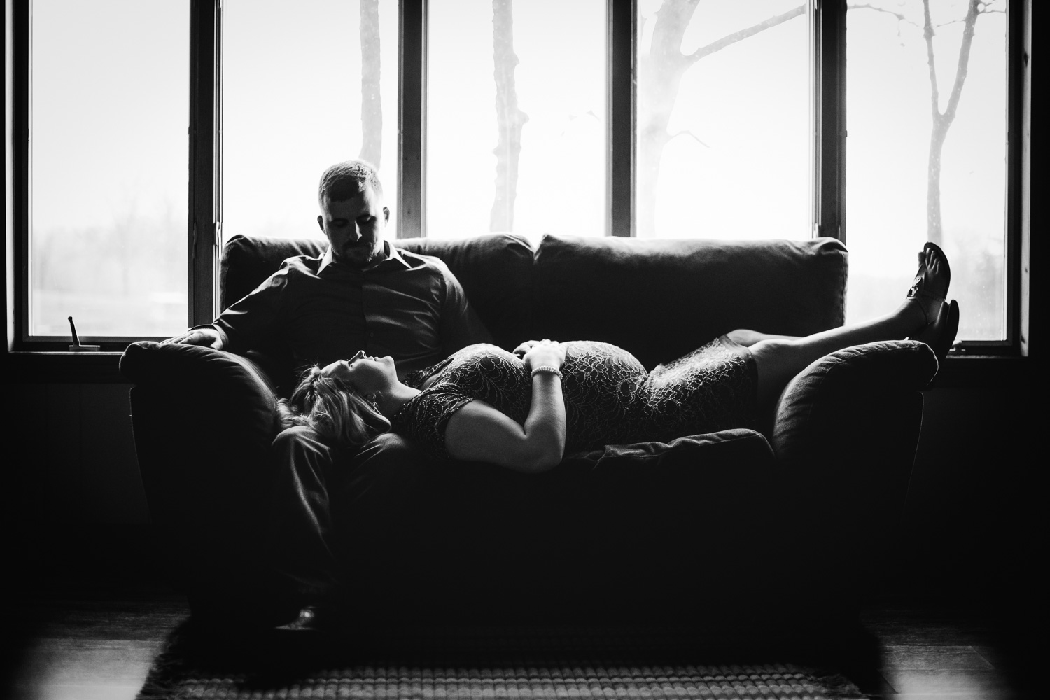 pregnant couple lounging on couch with wooded background