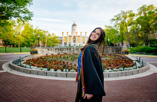 college graduate looks over shoulder near flowers and buildings