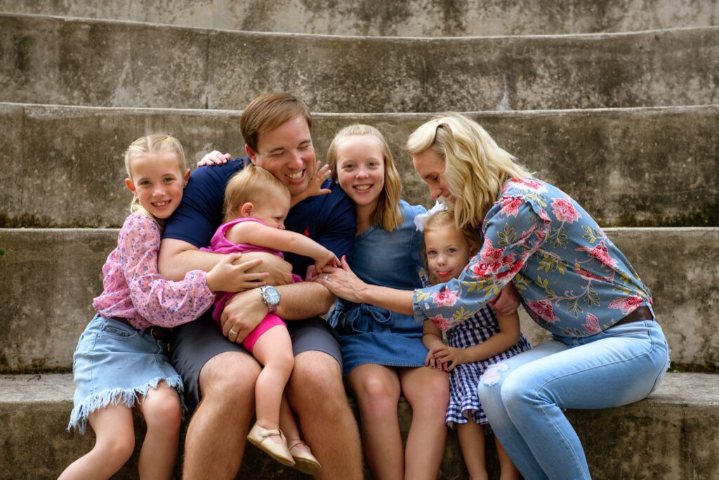 Drinkwitz Family snuggles youngest daughter while sitting on concrete steps.