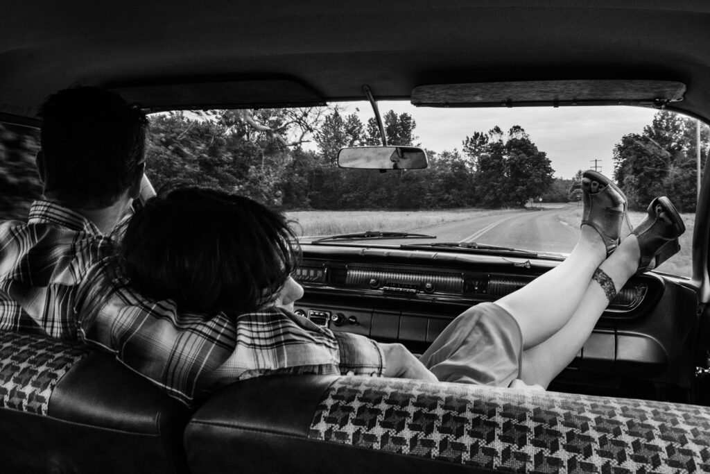 Woman snuggles to guy while driving car with her feet on the dash.