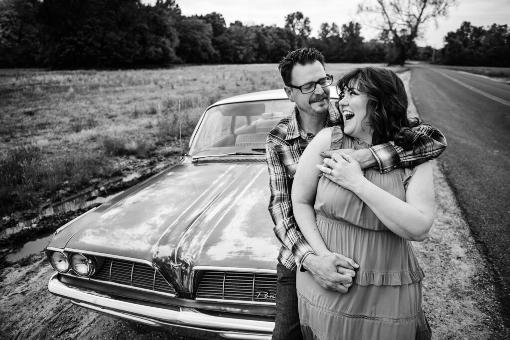 Couple cuddle together on the side of the road in front of car
