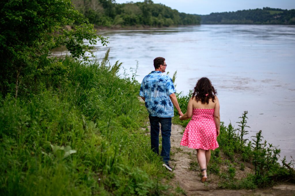 Engaged couple hold hands while walking next to the Missouri River.