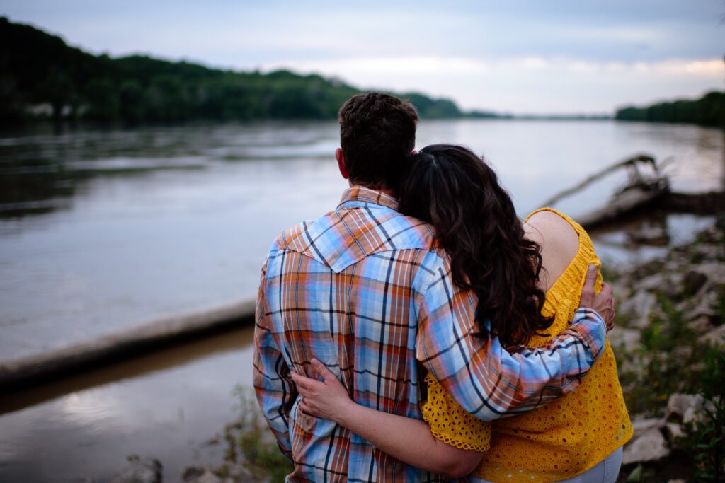 Engaged couple hug each other and lay head on shoulder.