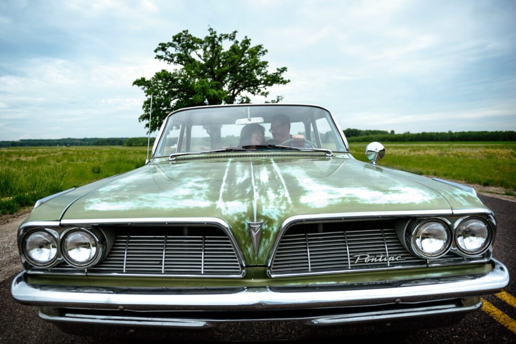 Couple sit in green Pontiac Catalina in front of a big tree