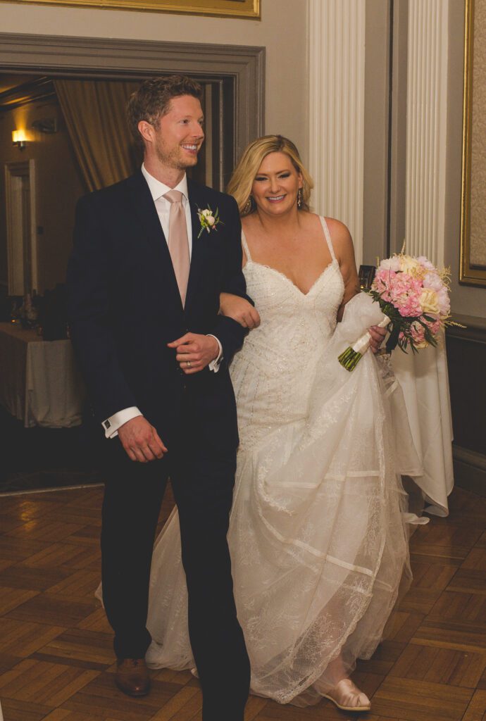 Scott and Shannon Schaefer smile as they walk arm and arm into their wedding reception at the tiger hotel in columbia, missouri.