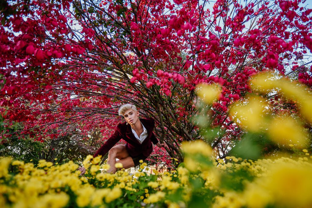 High School Senior Guy sits near red and yellow flowers