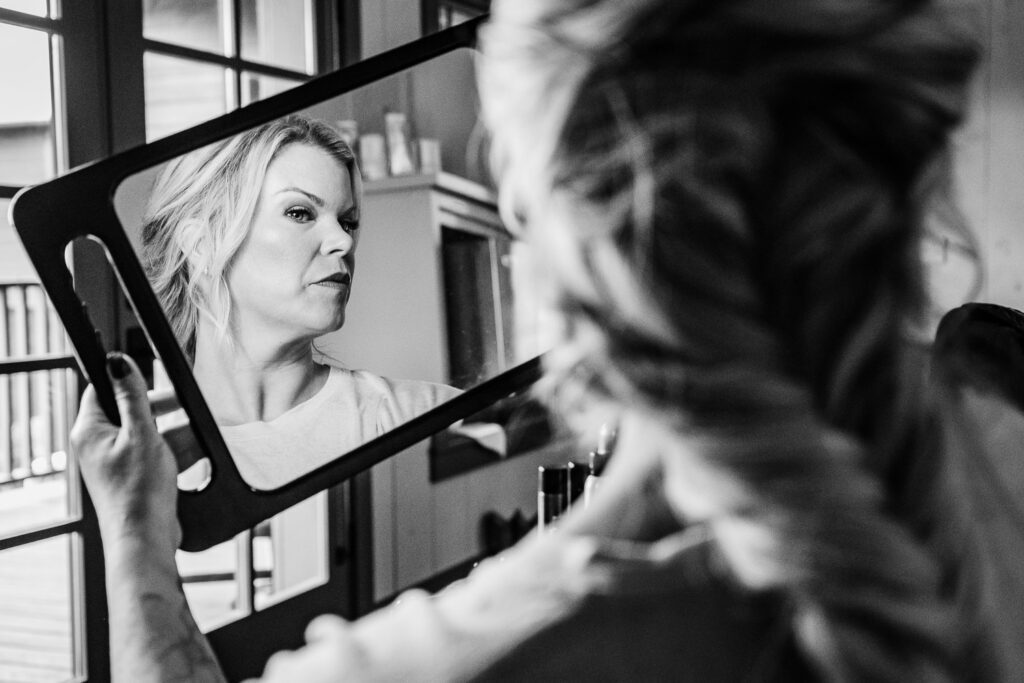 Bride looks at makeup in handheld mirror.