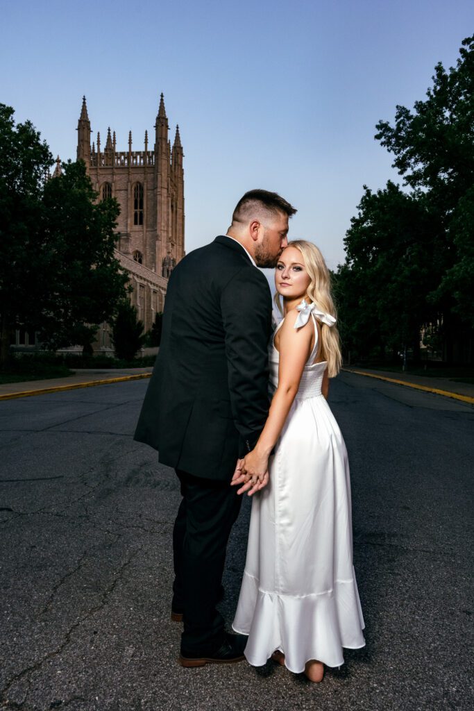 Engagement session in front of Memorial Union with guy kissing girl's forehead.