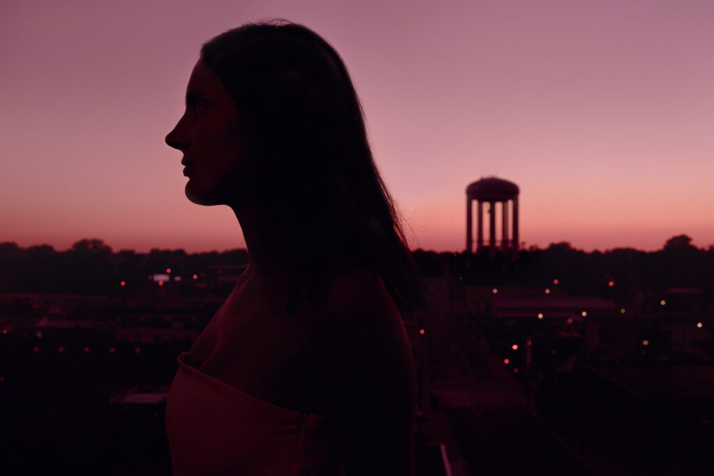 Silhouette of a girl with long hair and a water tower in downtown Columbia, Missouri with pink sky.