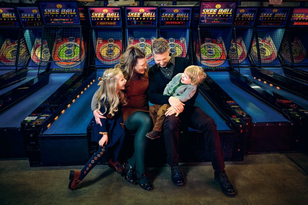 Family laughs while sitting on Ski Ball machines in Arcade.