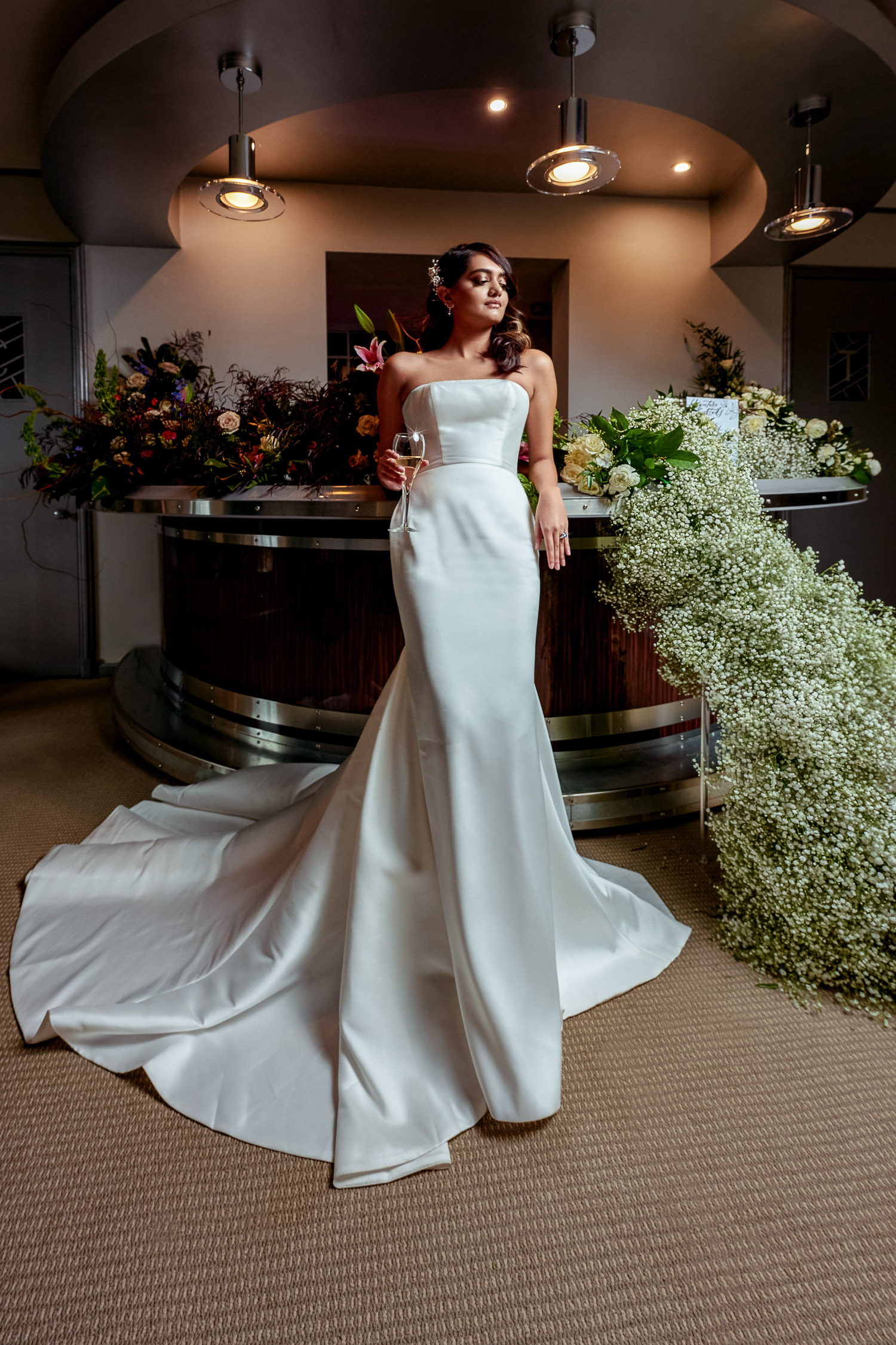 bride leaning against bar with glass of champagne and florals cascading down