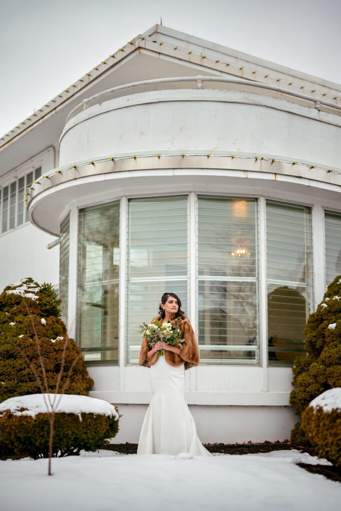bride standing in fur cape in front of The Chatol with snow on ground