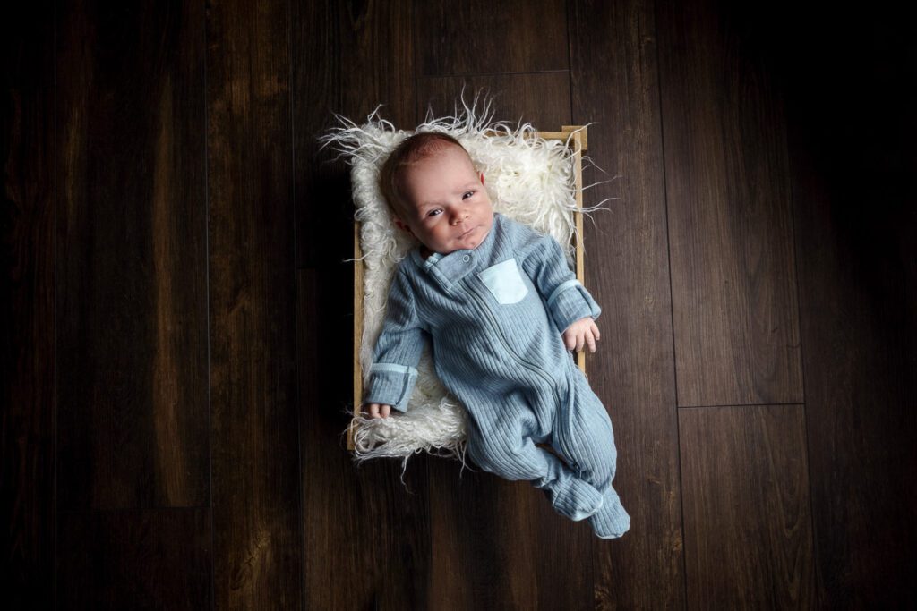 newborn baby wearing blue sits in small box