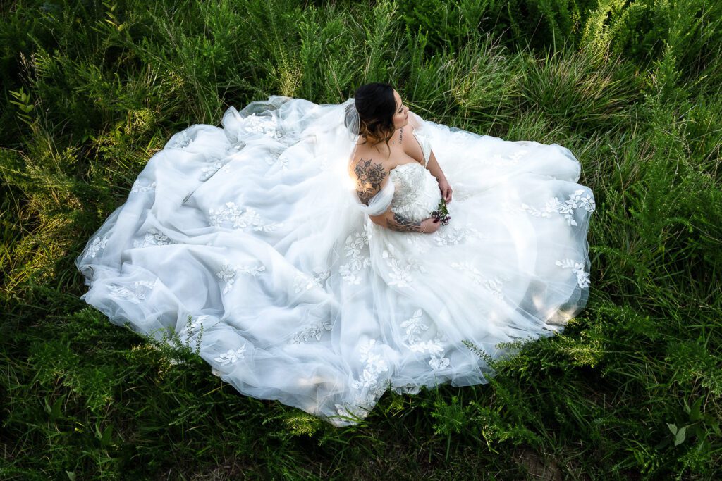 bride sitting in green grass with wedding dress spread out