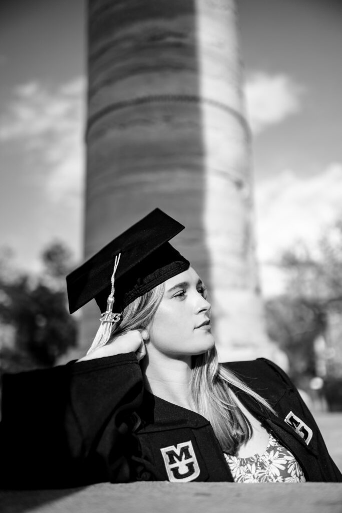 senior woman at mu wearing cap and gown leaning on mizzou column